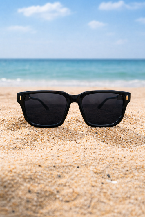 Black sunglasses on a sandy beach with ocean and blue sky in the background