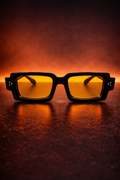 Sunglasses with yellow lenses on a dark surface with a warm glow