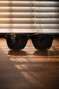 Black sunglasses on a wooden surface with blinds in the background