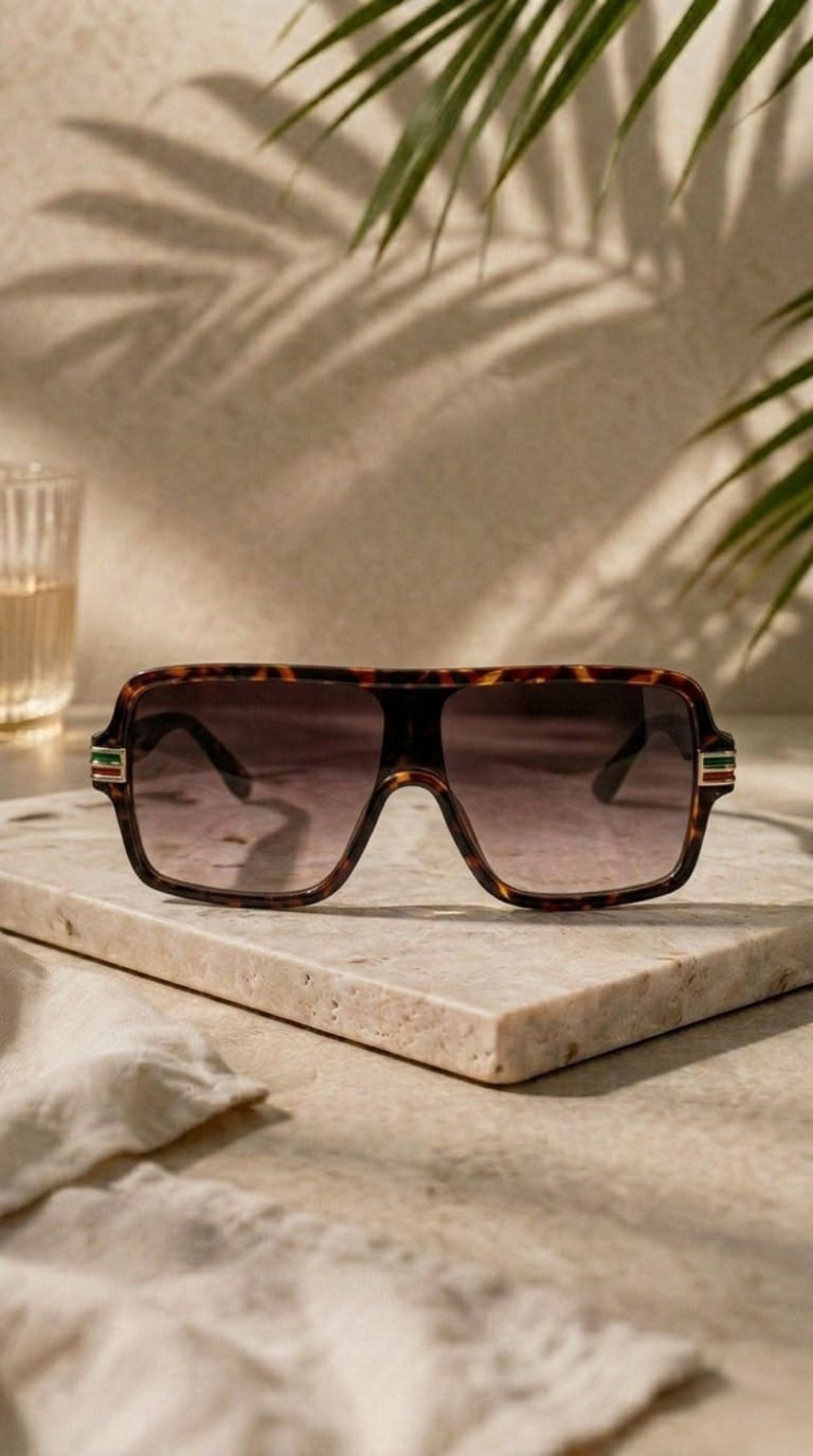 Sunglasses on a marble surface with a glass of water and plant in the background