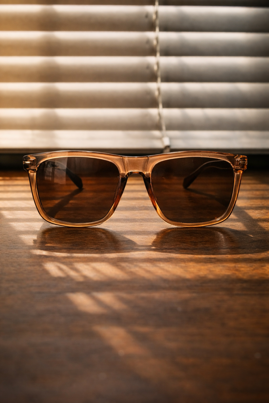 Brown sunglasses on a wooden surface with blinds in the background