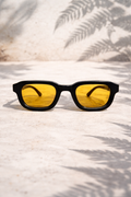 Sunglasses with yellow lenses on a textured surface with leaf shadows