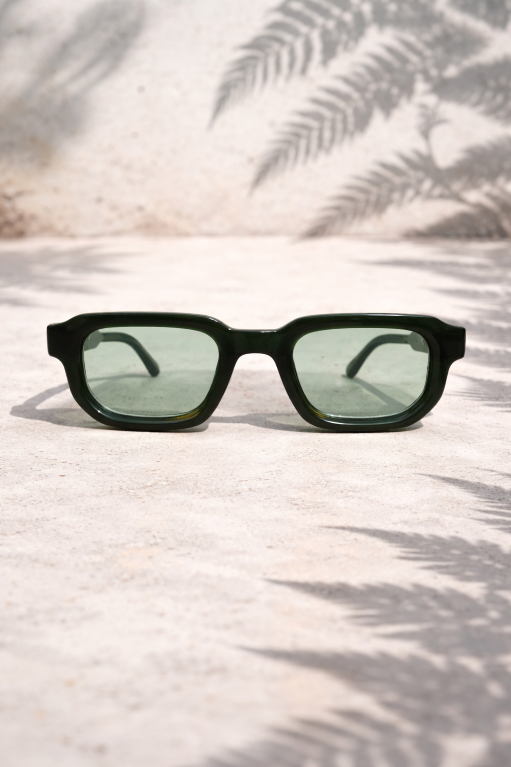 Black sunglasses with green lenses on a light surface with leaf shadows