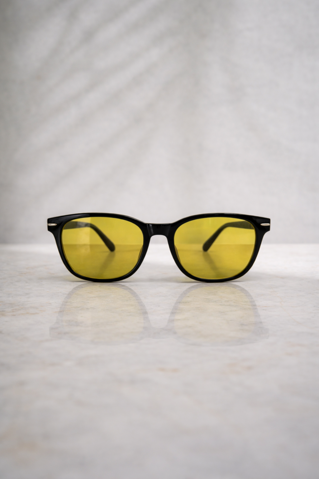 Sunglasses with yellow lenses on a reflective surface