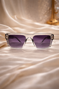 Clear-framed sunglasses with purple lenses on a satin surface