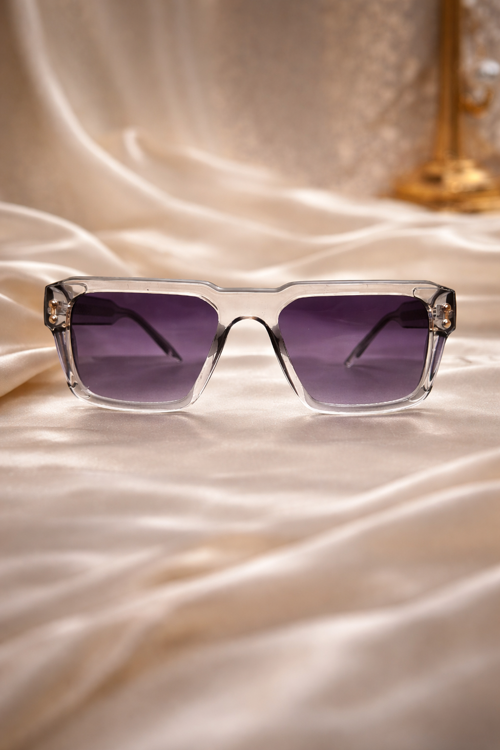 Clear-framed sunglasses with purple lenses on a satin surface
