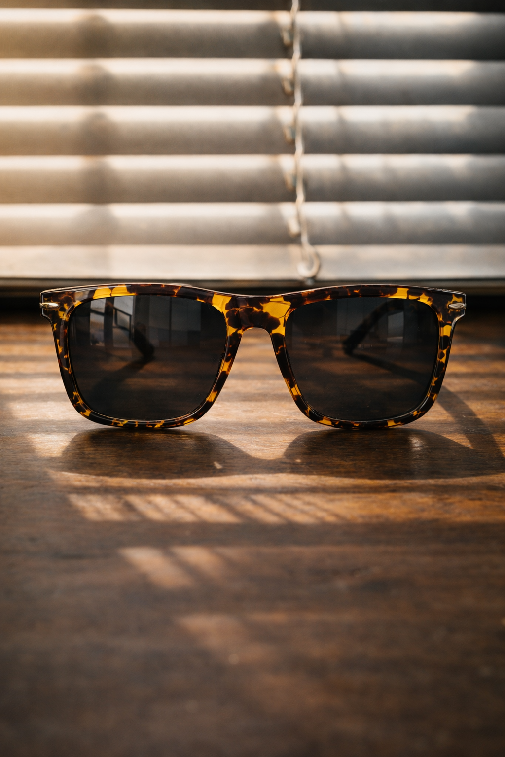 Tortoiseshell sunglasses on a wooden surface with blinds in the background
