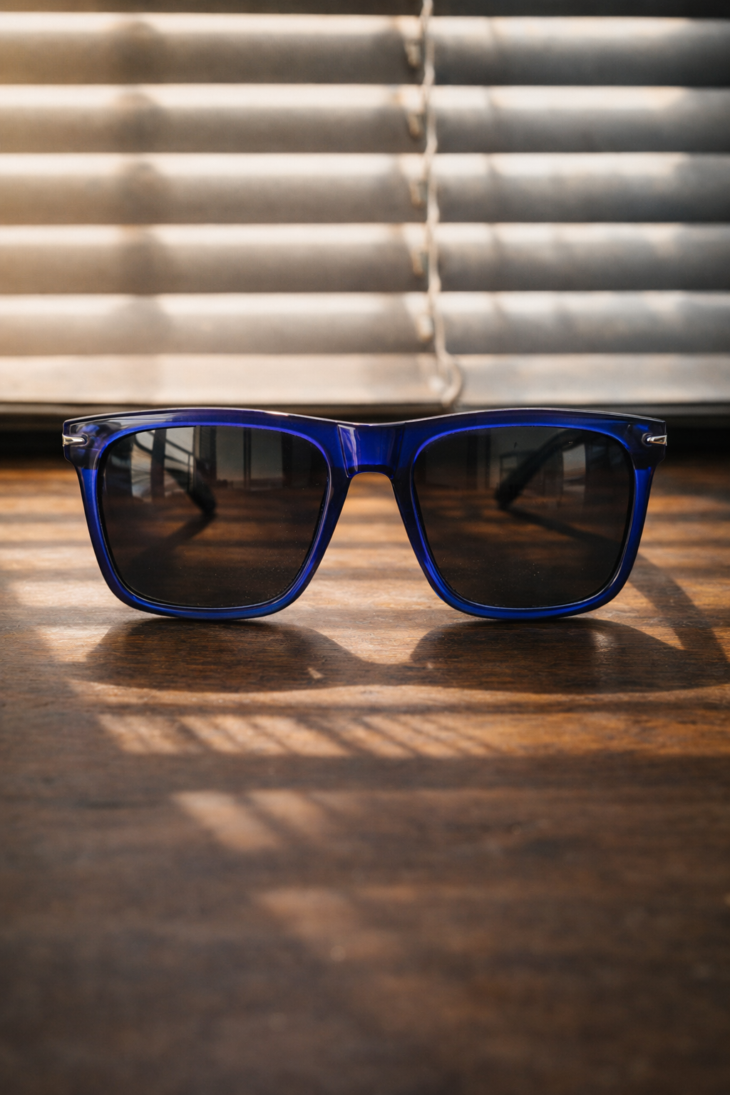 Blue sunglasses with dark lenses on a wooden surface with blinds in the background
